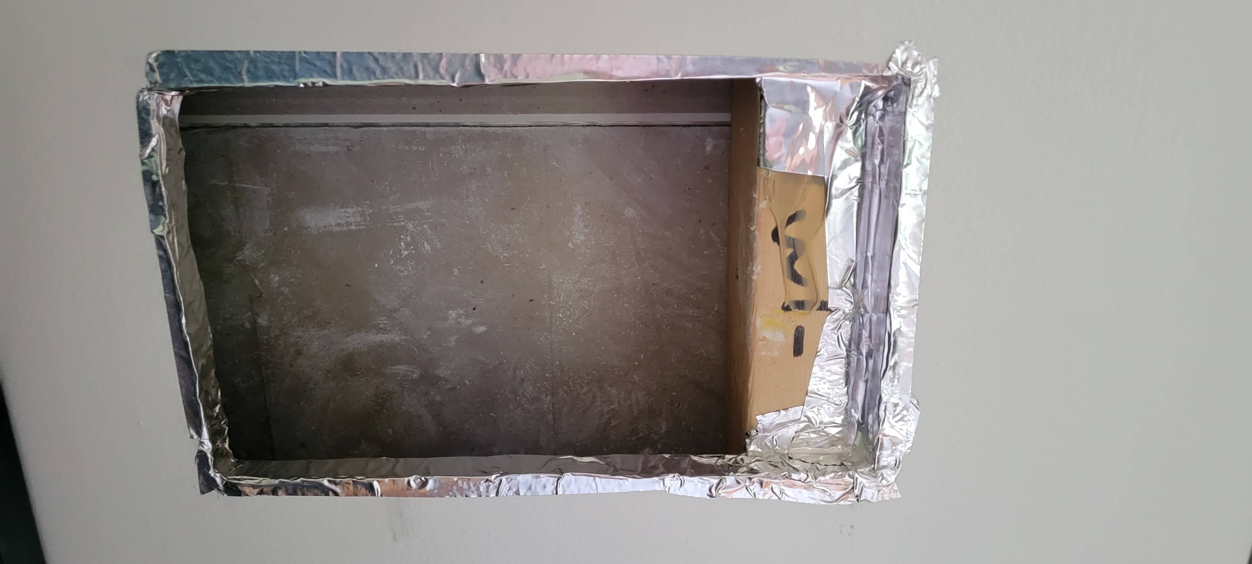 a rectangular hole in drywall with aluminum tape around the drywall edges