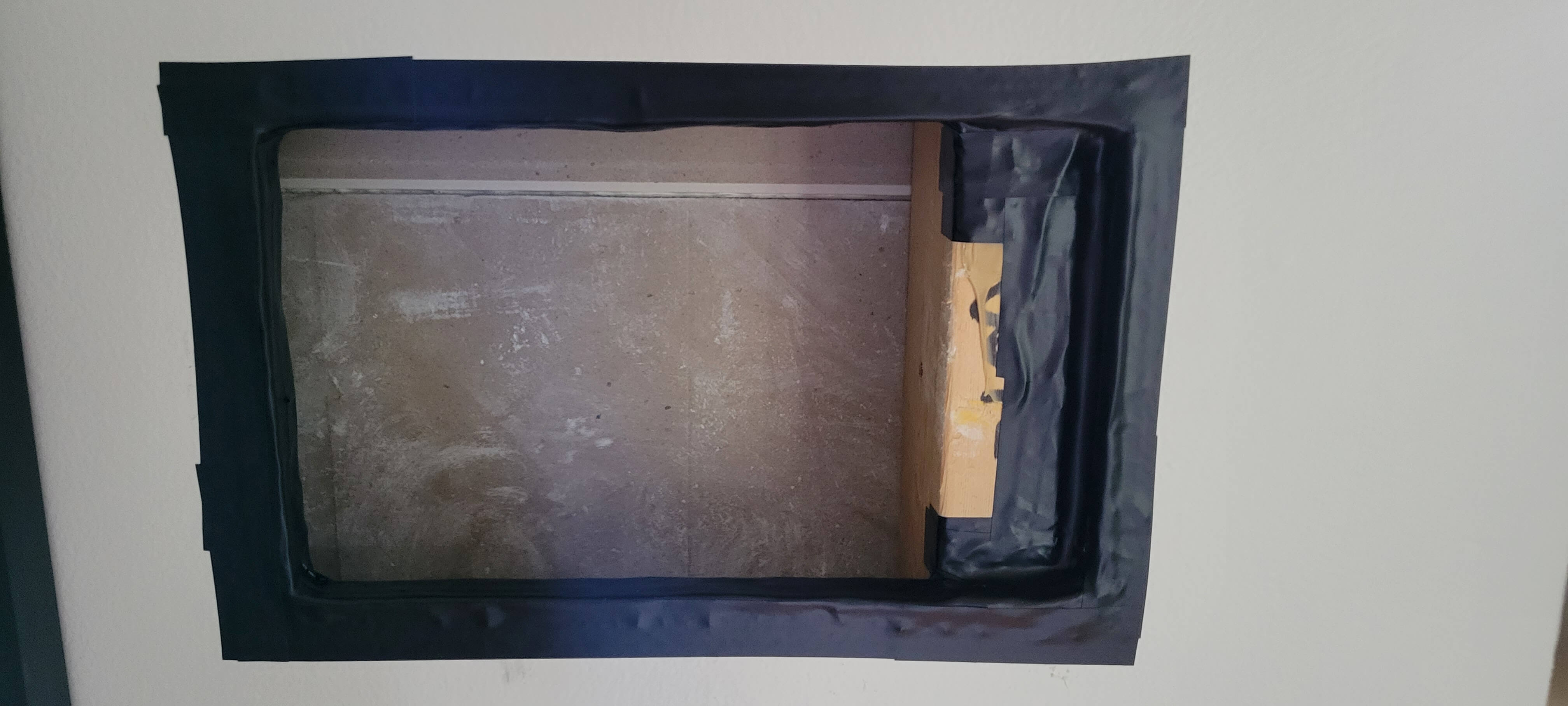 a rectangular hole in drywall with electrical tape around the drywall edges